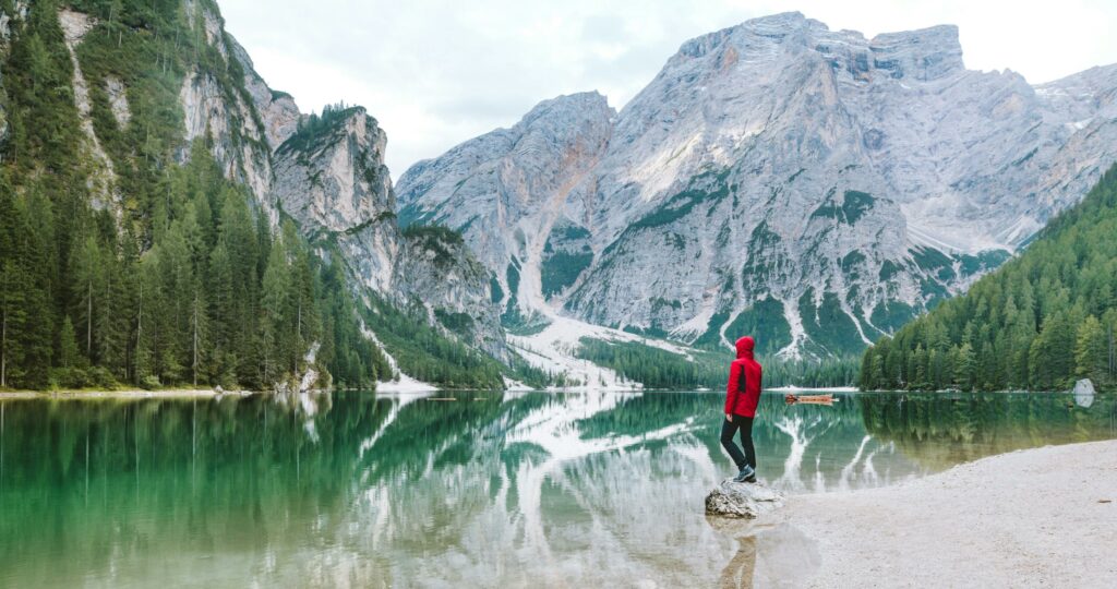 Person standing by the scenic Lake Braies with majestic Dolomite mountains reflected in the water.